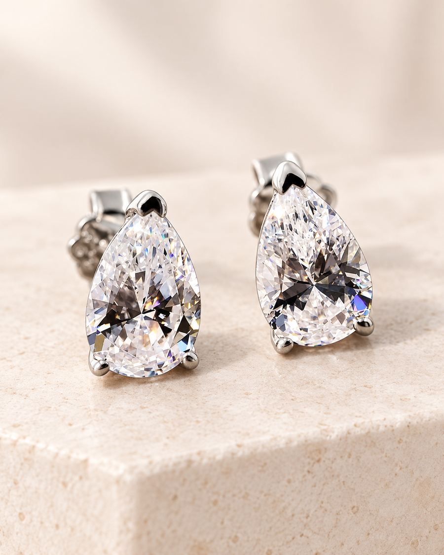 Elite pear-shaped clear solitaire stud earrings in silver on a warm ivory surface