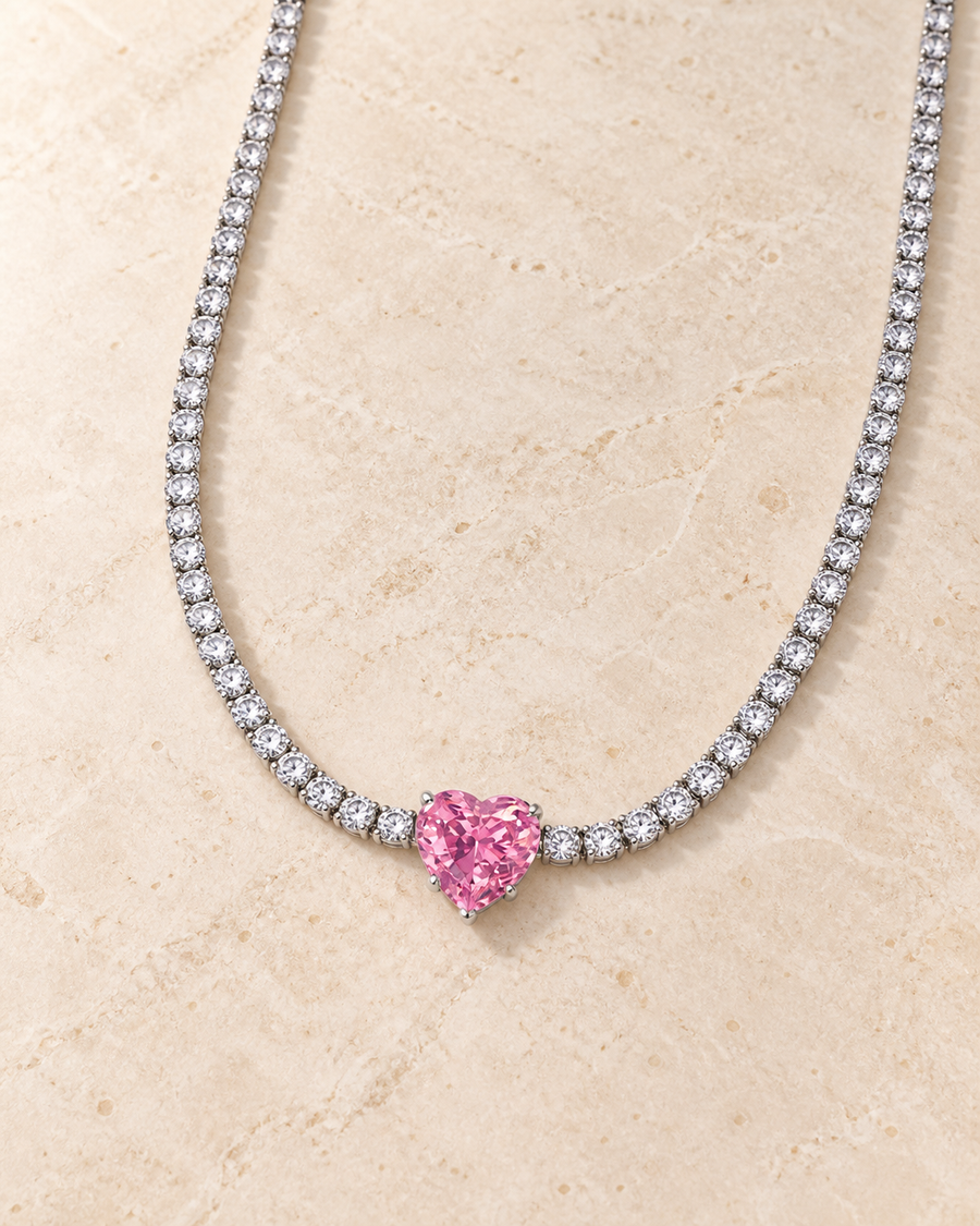 Heart FairyTale silver tennis necklace with one pink heart stone laid on an ivory tabletop