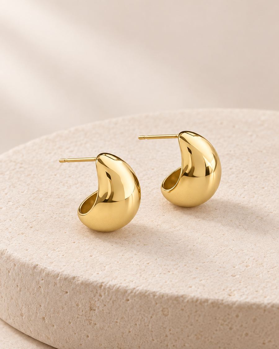 Gold Zenith Hoops with smooth rounded curves photographed on warm ivory stone